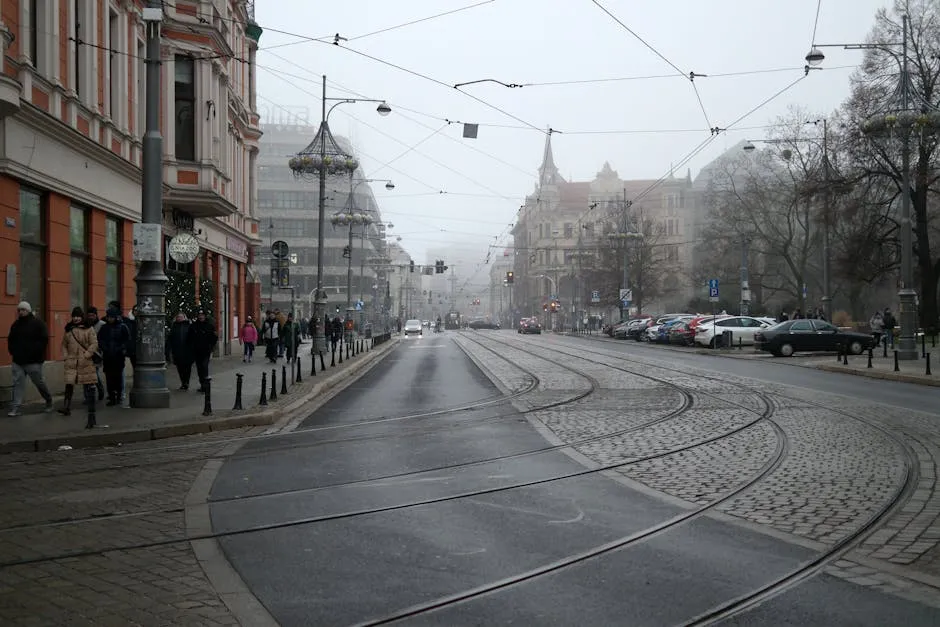 Foggy Polish city street with tram tracks, historic buildings, and pedestrians.